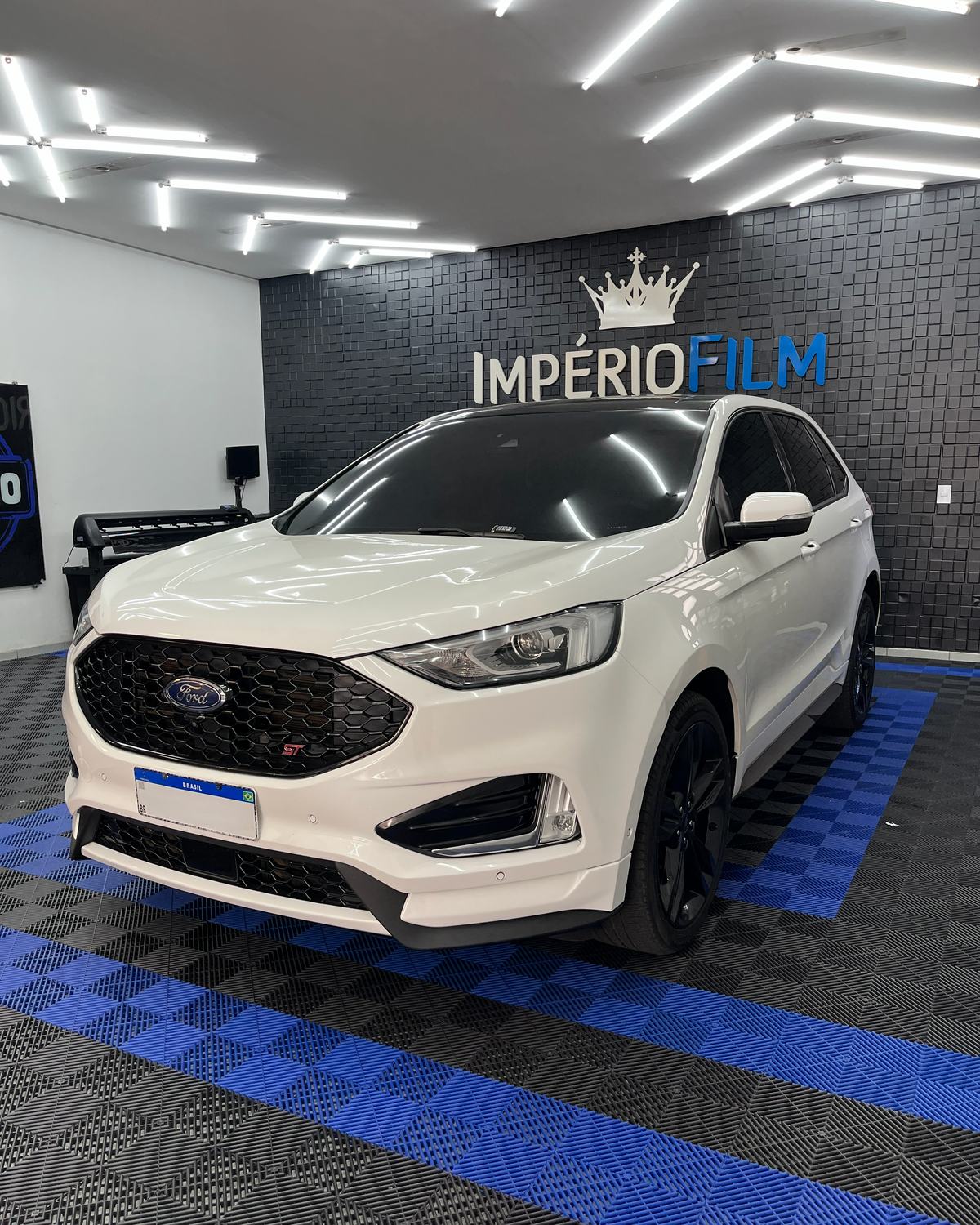 Interior da Império Film em Divinópolis: SUV no box de aplicação, com o logo na parede e o plotter de corte ao fundo